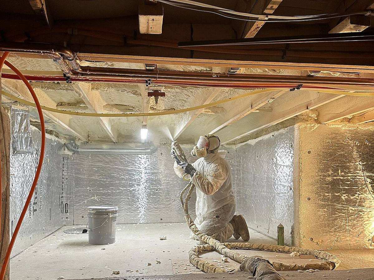 Technician applying spray foam insulation under floor joists in a Chattanooga-area home